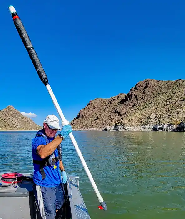 A crew member collecting a water sample using a long plastic tube.